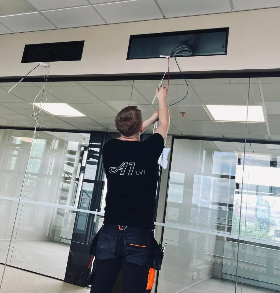 LVI-asentaja työskentelee kattoaukosta roikkuvien johtojen parissa suorittaen LVI-huoltoa.